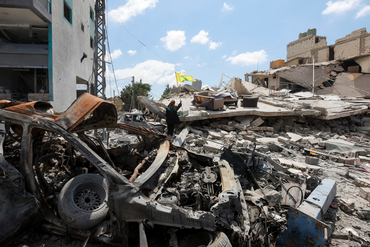 A woman holds a Hezbollah flag amid rubble of destroyed buildings, in Deir Qanoun al-Nahr, Tyre district, southern Lebanon,  June 15, 2026. REUTERS/Aziz Taher