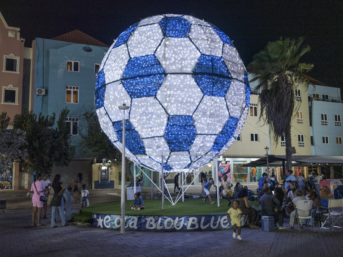 People gather near a big soccer ball that decorates Willemstad, Curacao, June 5, 2026. .Downtown Willemstad has had a celebratory fervor as the World Cup has kicked off. Competing for the first time in the World Cup soccer tournament, Curacao is brimming with joy. (Luis Antonio Rojas/The New York Times)