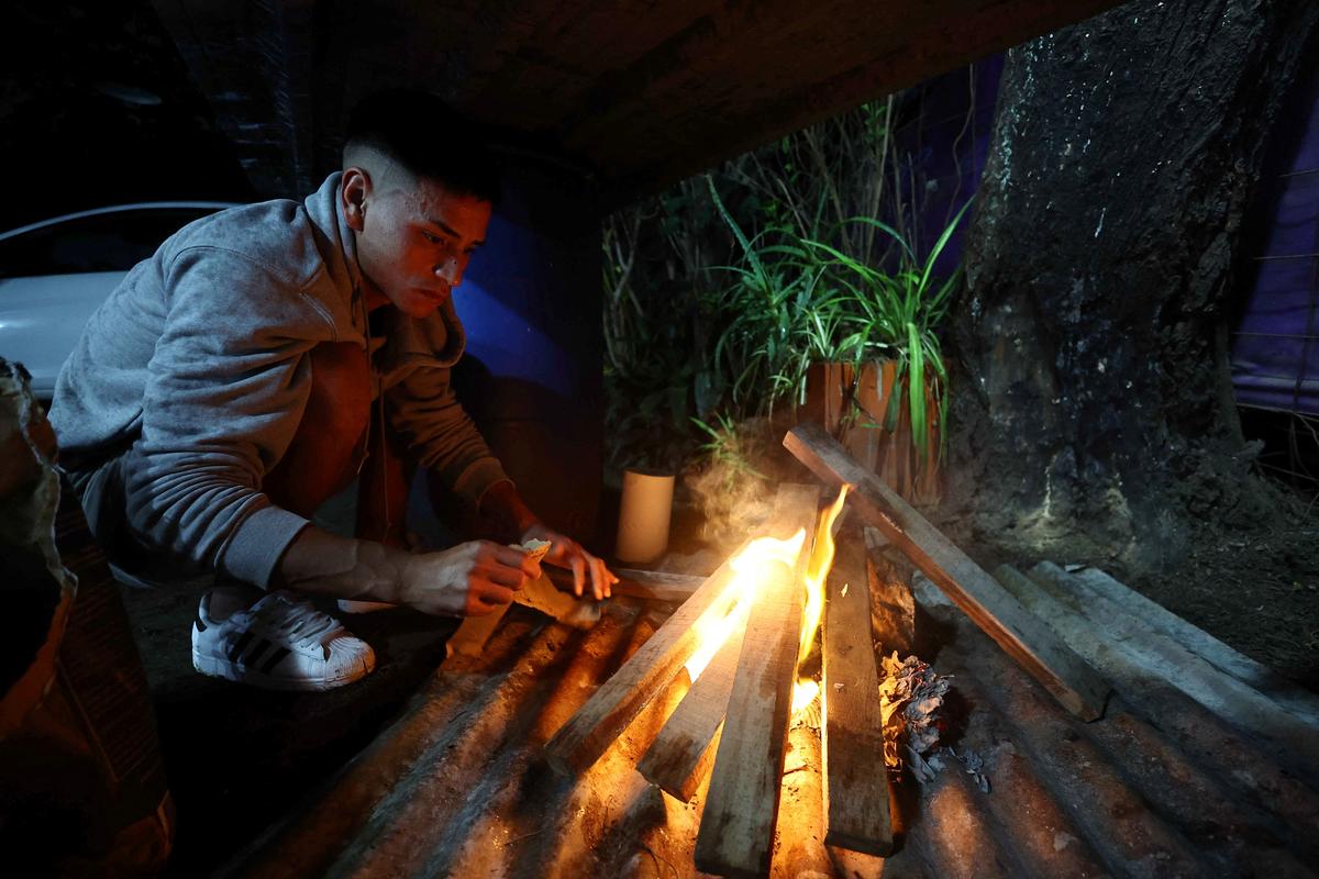 Emiliano Migueles, 26, lights a fire to cook a stew at a friend's house ahead of a weekly dinner with friends in the Parque San Martin neighbourhood in Merlo, on the outskirts of Buenos Aires, Argentina, April 20, 2026. Migueles starts his days early, delivering water. But his true grind begins when he clocks out and hits the scrappy soccer pitches that dot the suburbs of Buenos Aires, pouring his energy into amateur football to earn extra cash. REUTERS/Agustin Marcarian