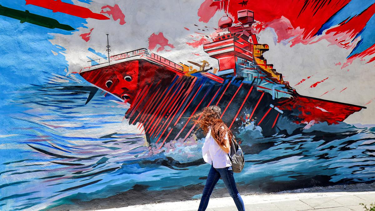 A woman walks past an anti-US and anti-Israel mural depicting missiles hitting an aircraft carrier in Tehran on May 26, 2026. US forces launched overnight strikes on missile sites in Iran and boats they said were trying to lay mines in Gulf waters, sending oil prices higher on May 26, while diplomats sought a deal to end the war. Iran did not immediately confirm the reported strikes, but state media reported blasts in the southern port city of Bandar Abbas, and the Revolutionary Guards Corps said its forces had downed a US drone entering its airspace and fired at an F-35 fighter jet. (Atta Kenare/AFP/Getty Images/TNS)