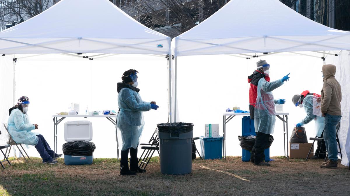 Workers, left, change their medical gloves as people are tested for COVID-19 at a walk-up testing site at Farragut Square, Thursday, Dec. 23, 2021, just blocks from the White House in Washington. The worldwide surge in coronavirus cases driven by the new omicron variant is the latest blow to hospitals, police departments, supermarkets and other critical operations struggling to maintain a full contingent of front-line workers as the pandemic enters its third year. (AP Photo/Jacquelyn Martin)