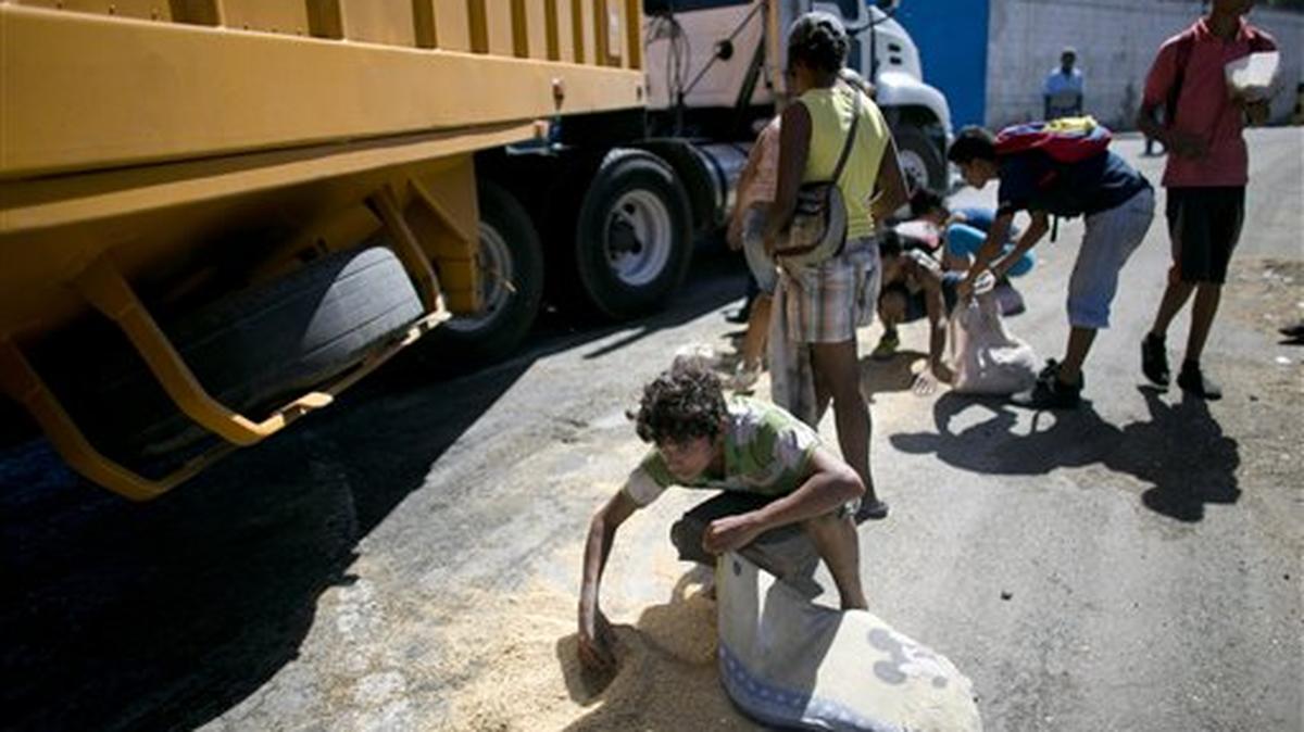 En esta imagen de archivo, tomada el 14 de noviembre de 2016, un niño emplea la funda de una almohada como bolsa para guardar arroz caído al suelo de un camión de carga que esperaba para entrar al puerto de Puerto Cabello, Venezuela, el lugar desde donde se gestionan la mayoría de las importaciones de alimentos de Venezuela. Mientras millones de venezolanos pasan hambre, el contrabando de comida se ha convertido en uno de los negocios más lucrativos en el país.
