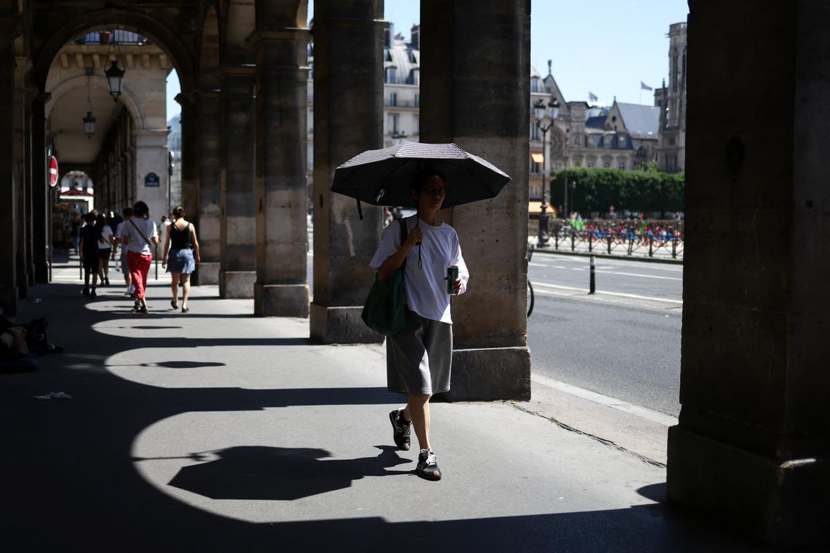 A person shelters under an umbrella outside the Louvre amid a heatwave in Paris, France, May 27, 2026. REUTERS/Tom Nicholson