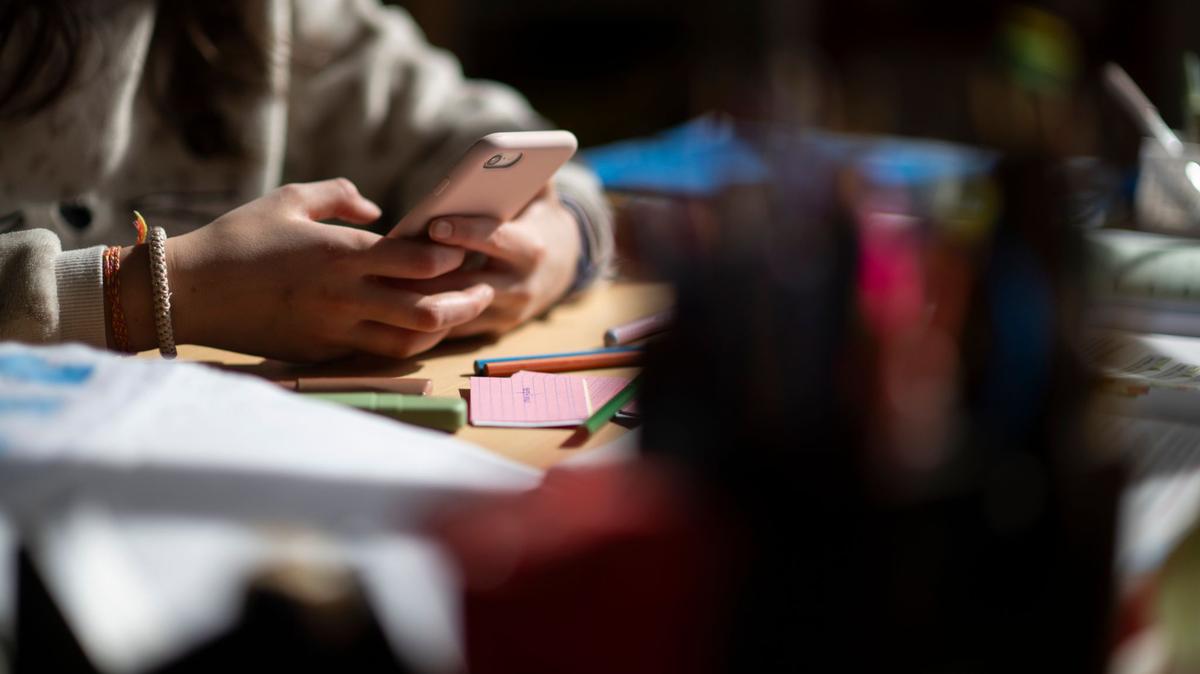 A child sits at a desk with school supplies, holding a smartphone in their hands in a staged scene. (Marijan Murat/dpa/TNS)