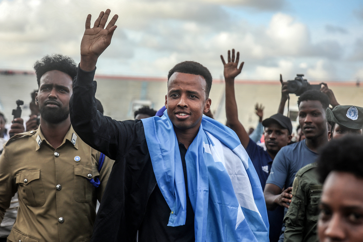  TOPSHOT – Somali international referee Omar Abdulkadir Artan waves to supporters while draped in the Somali flag as he is welcomed ahead of a solidarity football match after returning to Somalia in Mogadishu on June 10, 2026. Somali referee Omar Artan, who was denied entry to the United States for the World Cup, returned to a hero’s welcome in Mogadishu and vowed to take part in the next tournament in 2030. Artan’s rejection has sparked outrage at home.Artan, who in 2025 was named men’s referee of the year by the Confederation of African Football (CAF), was barred from entering the US on Saturday after arriving at Miami International Airport. (Photo by Hassan Ali Elmi / AFP via Getty Images) 