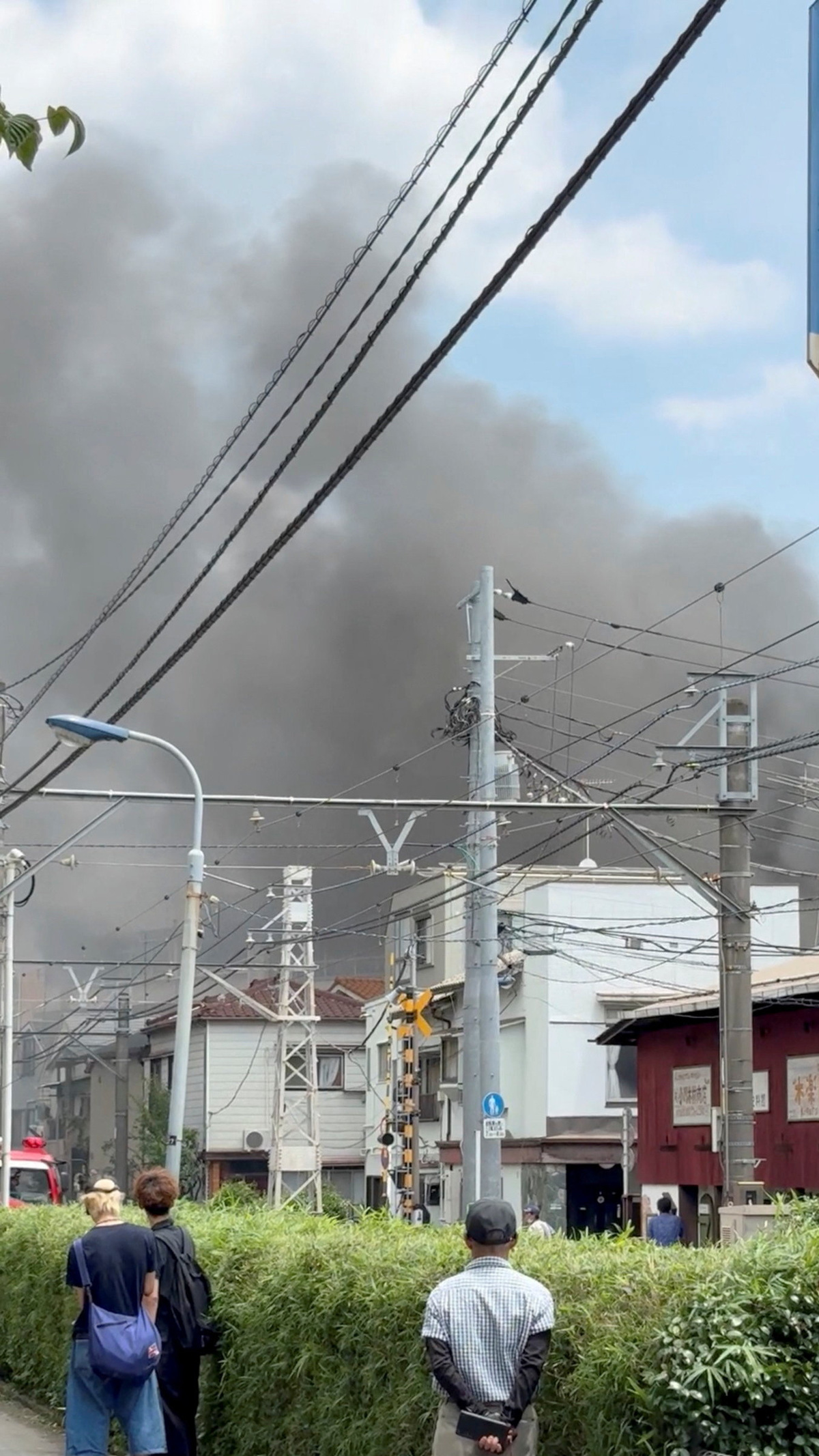 People watch smoke rising from a fire at a primary school in Tokyo, Japan, June 19, 2026, in this still image obtained from social media video. @Ayuthin0217 via X/via REUTERS