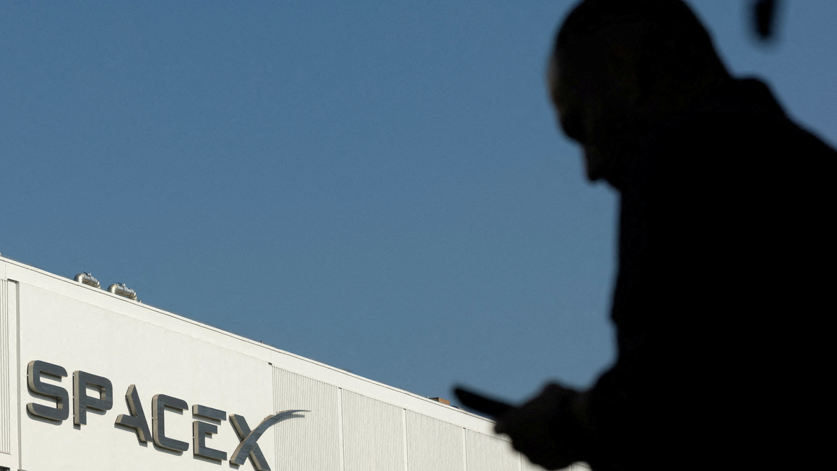 FILE PHOTO: SpaceX logo as an employe looks at his phone while making his way to work at the company’s facility on the day of the SpaceX IPO, in Hawthorne, California, U.S. June 12, 2026.  REUTERS/Mike Blake/File Photo