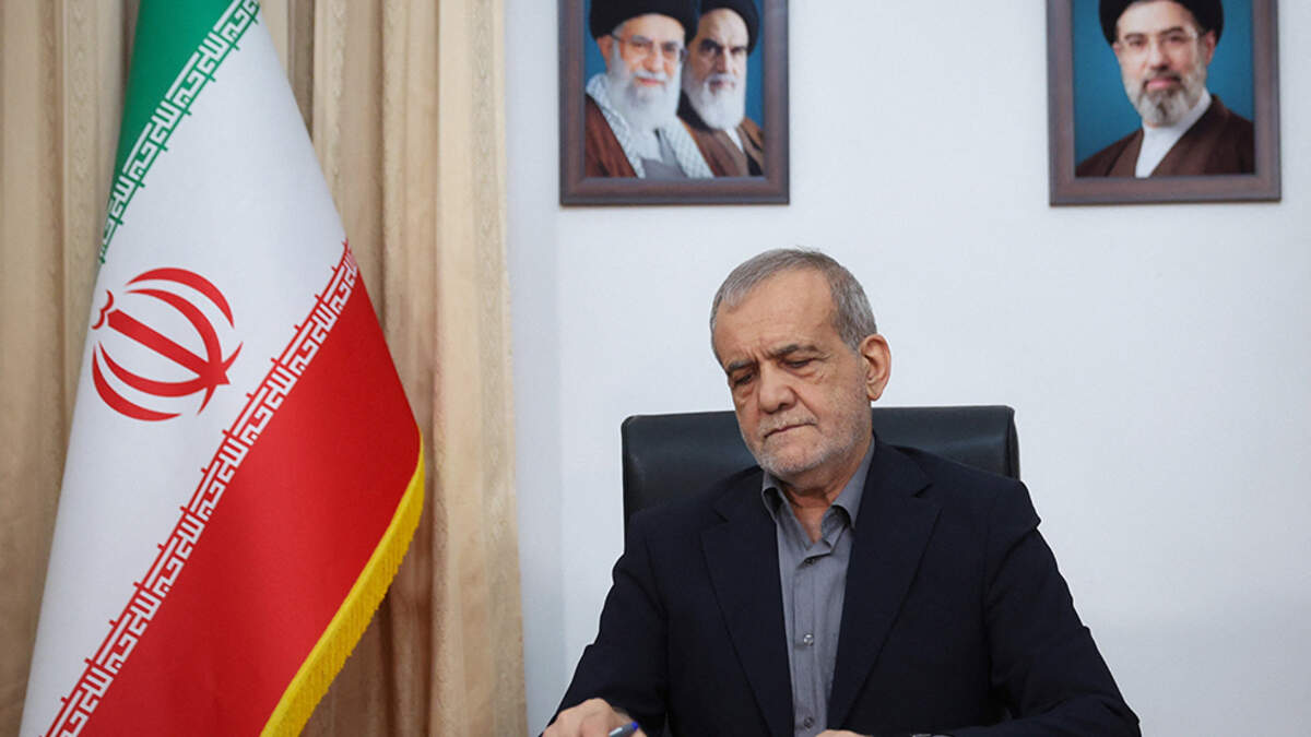 With portraits of the current and former Iranian supreme leaders behind him, President Masoud Pezeshkian signs the document of the Memorandum of Understanding with the U.S. in Tehran on Thursday.