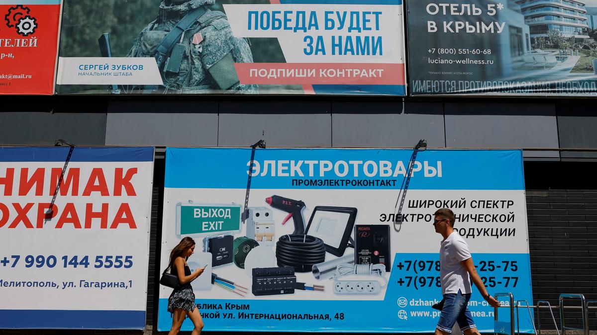 People walk past a banner promoting a contract military service in the Russian armed forces, amid Russia-Ukraine conflict in the city of Melitopol in the Zaporizhzhia region, a Russian-controlled area of Ukraine, August 14, 2025. REUTERS/Alexander Ermochenko