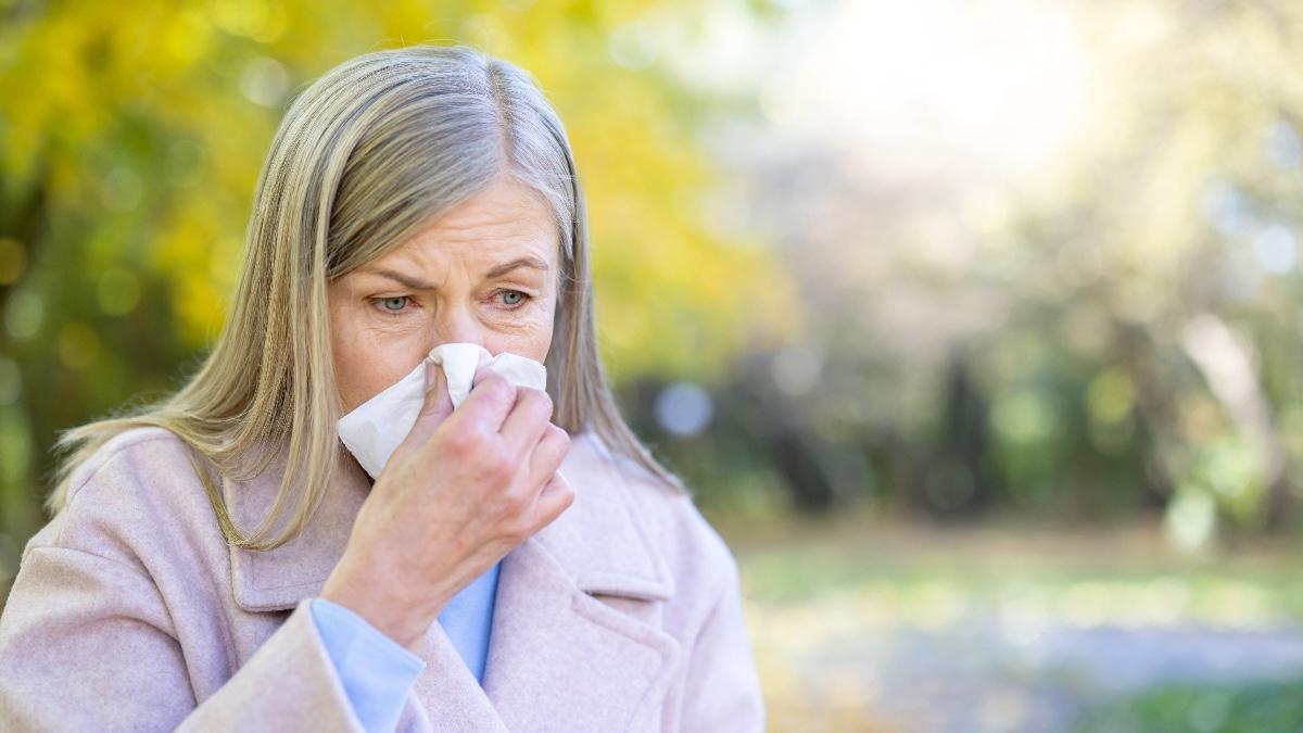 Senior woman blows her nose into a tissue while standing in an autumn park. HMPV infections are most common during winter through spring, the CDC said.