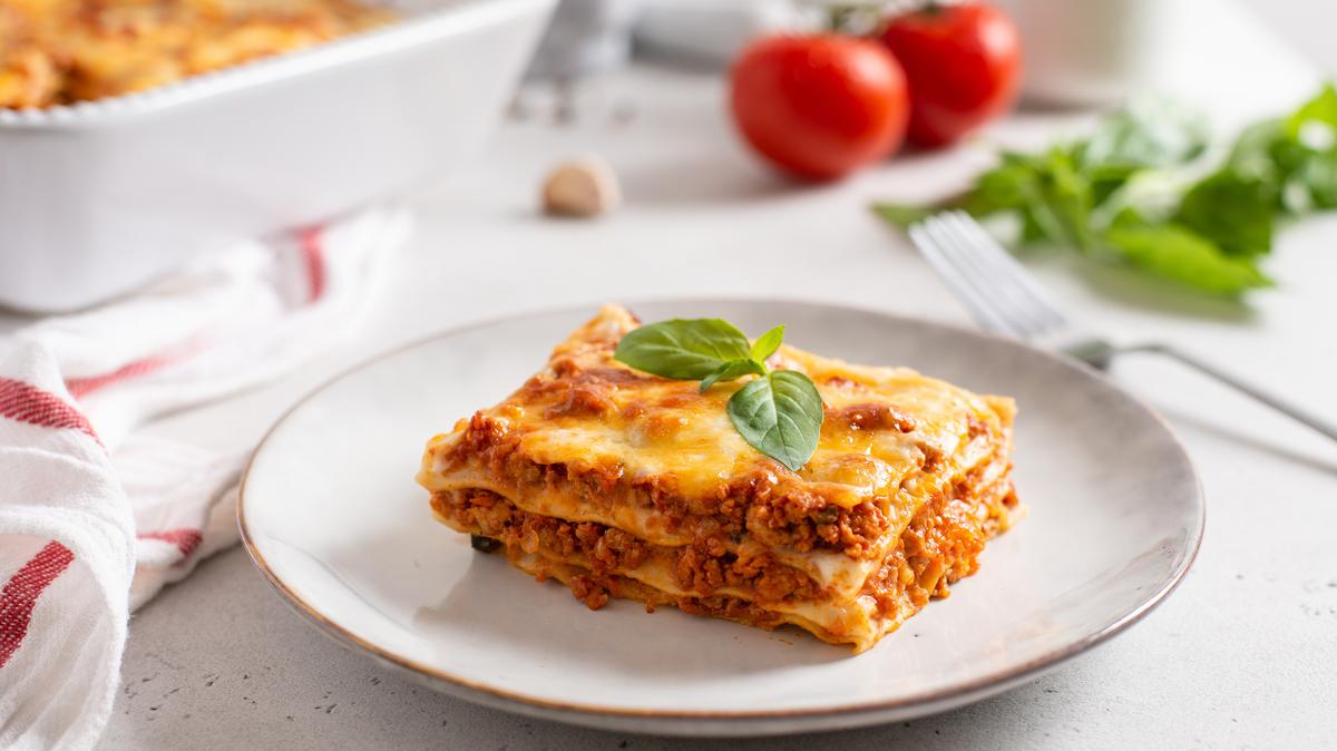 Piece of tasty hot lasagna served with a basil leaf on a gray plate. Italian cuisine, menu, recipe. Homemade meat lasagna. Close up, side view