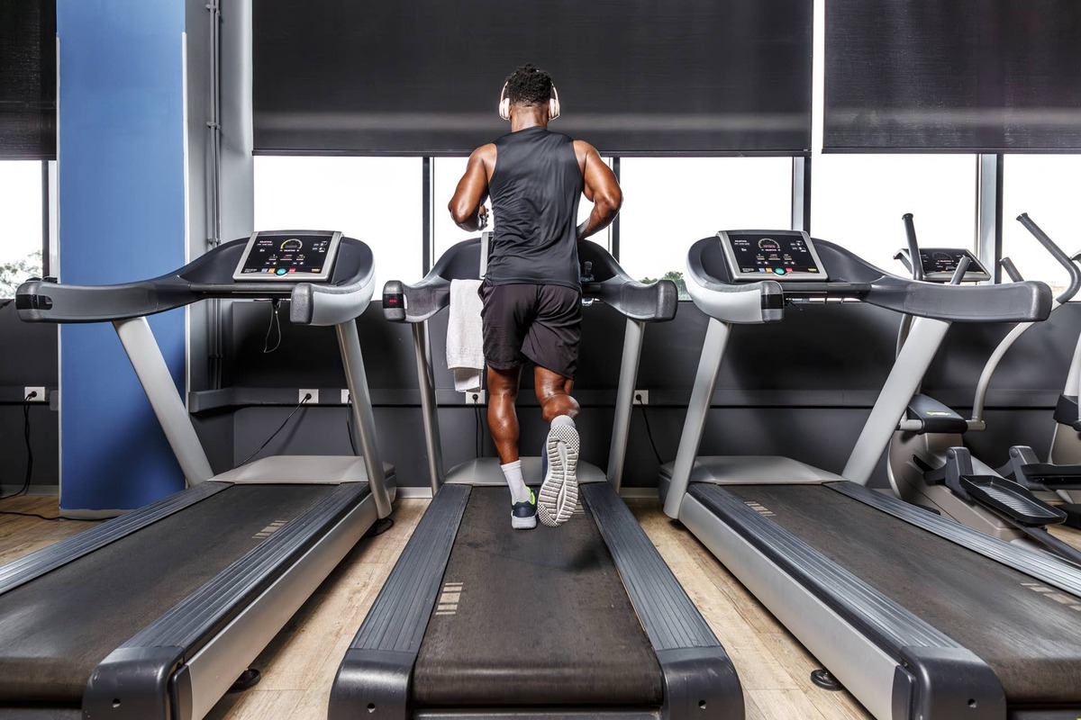  A man is energetically running on a treadmill in a gym. The gym is well-lit and equipped with various exercise machines, including the treadmill. The man is wearing workout clothes and appears focused on his exercise routine.