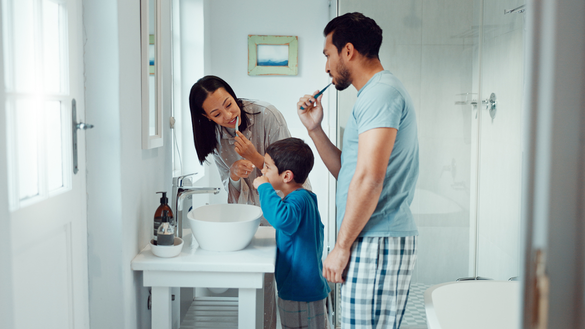 A stock image of parents, child and brushing teeth in family home bathroom while learning or teaching dental hygiene. 