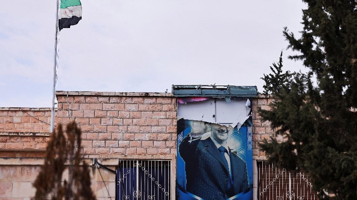 A torn poster of Syria's Bashar al-Assad hangs near the flag adopted by the new Syrian rulers, in Daraa, Syria, December 27, 2024. REUTERS/Zohra Bensemra