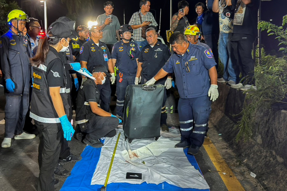 Rescue workers and forensic technicians with a suitcase, in which police later found the body of a 17-year-old Thai girl, for examination, after it was recovered from a grassy area near a railway track in Pattaya City, Thailand, June 27, 2026. . REUTERS/Teerasak Suttativong.
