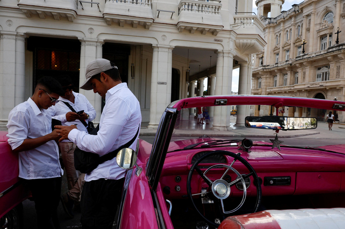 Taxi drivers of vintage cars look at their mobile phones while waiting for clients at Central Park, as U.S. sanctions have led most major tourism and travel companies to leave the island or drastically scale back their operations, in Havana, Cuba June 8, 2026. REUTERS/Norlys Perez