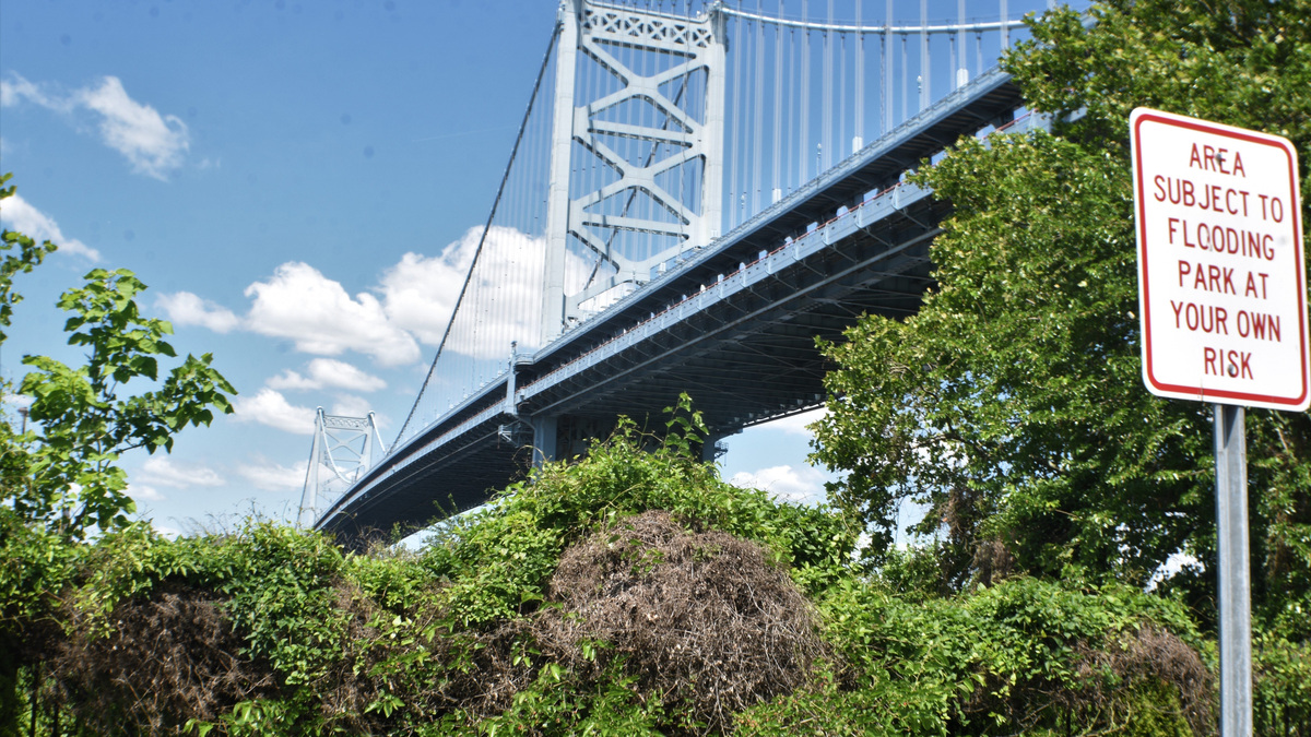 A PATCO train speeds across the Ben Franklin Bridge, which this month is celebrating its 100th anniversary. A parking-lot sign warns against parking near the Delaware River, which passes under the nearby Ben Franklin Bridge.