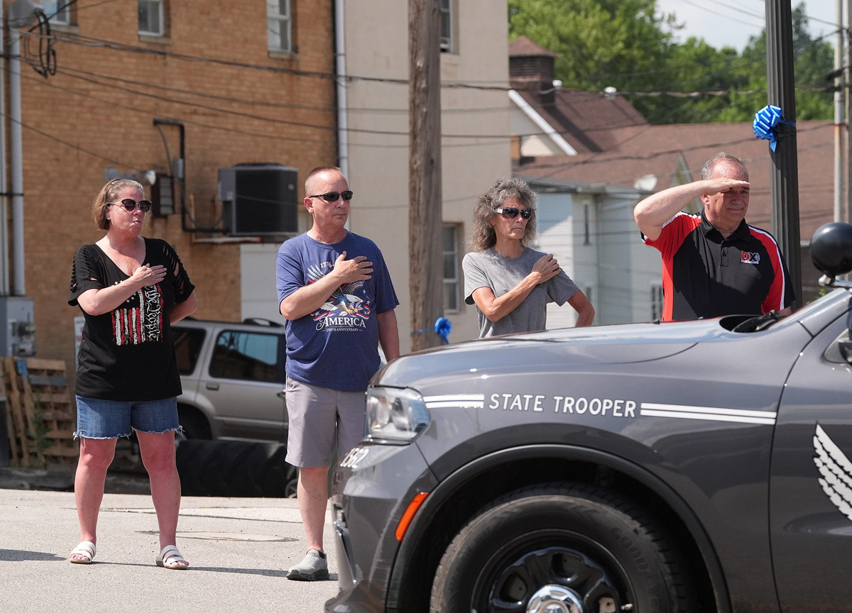 People stand in honor of Rittman police officer sgt. Scott Ries, as the watch the procession of Police vehicles that escorted Sgt. Ries along Ohio Avenue in Rittman, Ohio on July 6, 2026.