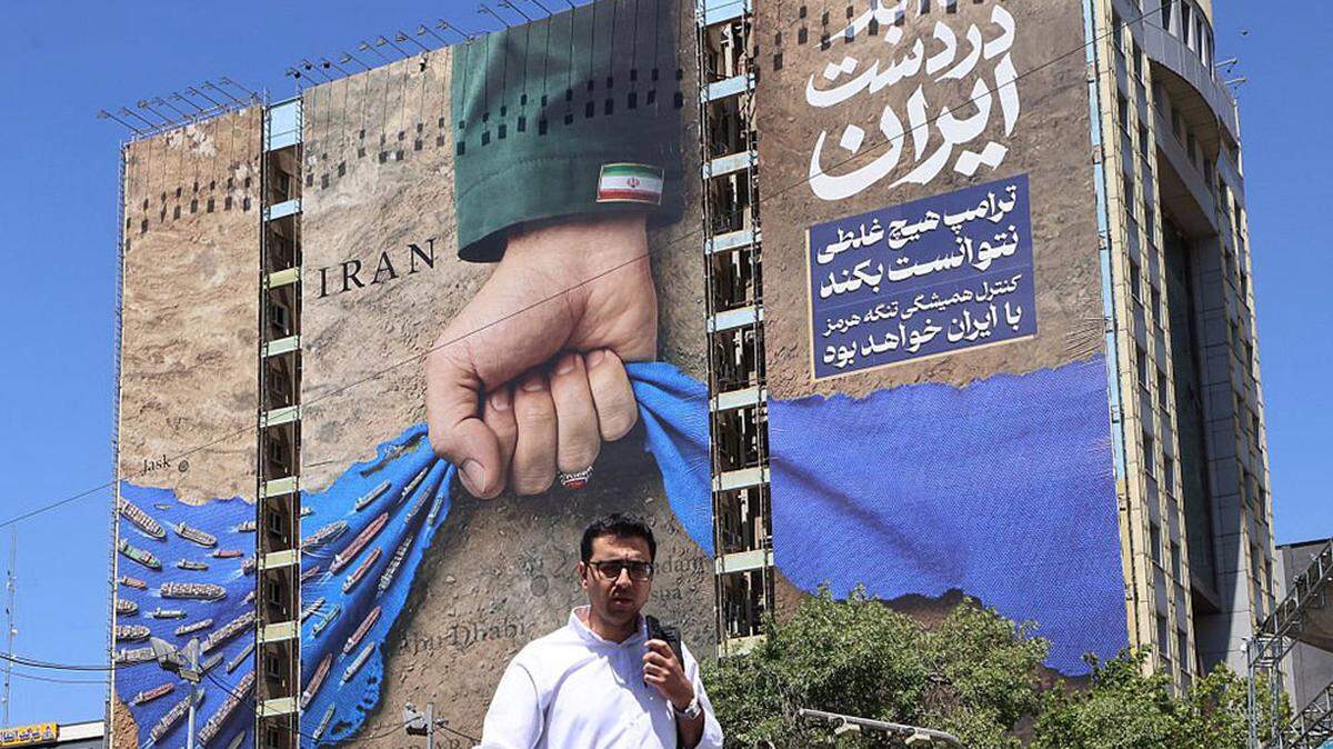A man crosses a street past a billboard on a building depicting the Strait of Hormuz with a caption in Persian reading, "Forever in Iran's Hand," at Vanak Square in Tehran on Monday. As Iranian officials were in Doha to hold talks with Qatar to end the three-month-old war, U.S. forces conducted strikes in southern Iran against targets, including boats attempting to lay mines and missile launch sites.