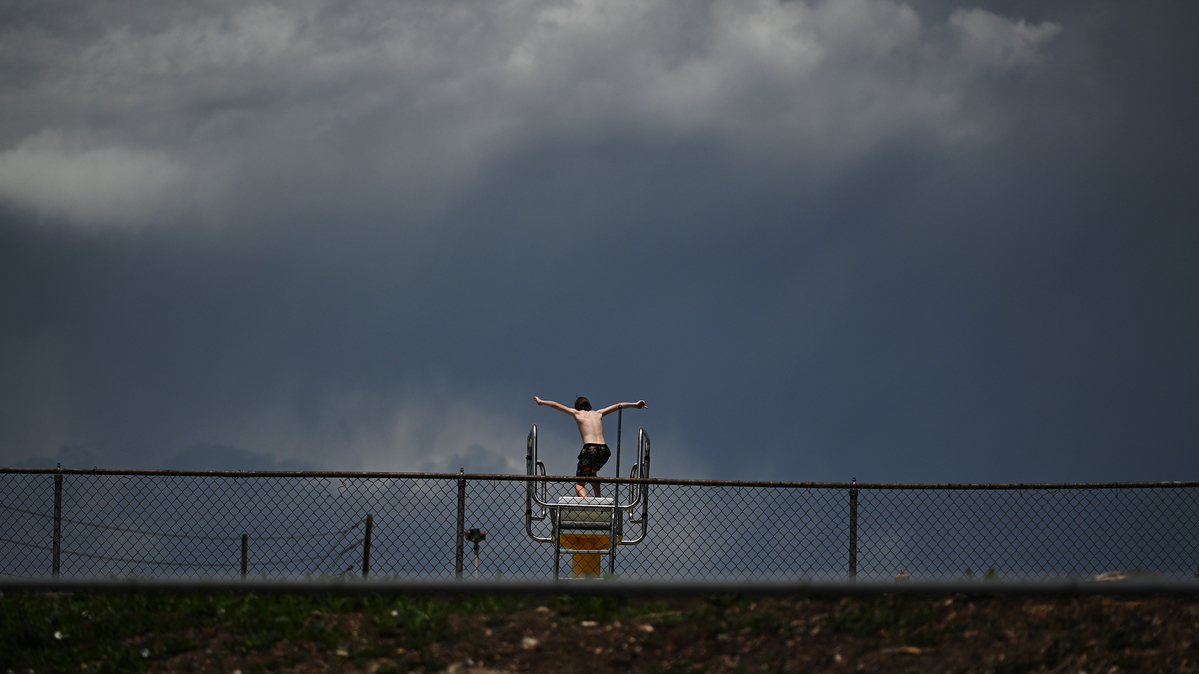 A boy jumps from a diving board at Green Mountain Swim Club as dark clouds move into the area from the west on June 2, 2026, in Lakewood, Colorado. (RJ Sangosti/The Denver Post/TNS)