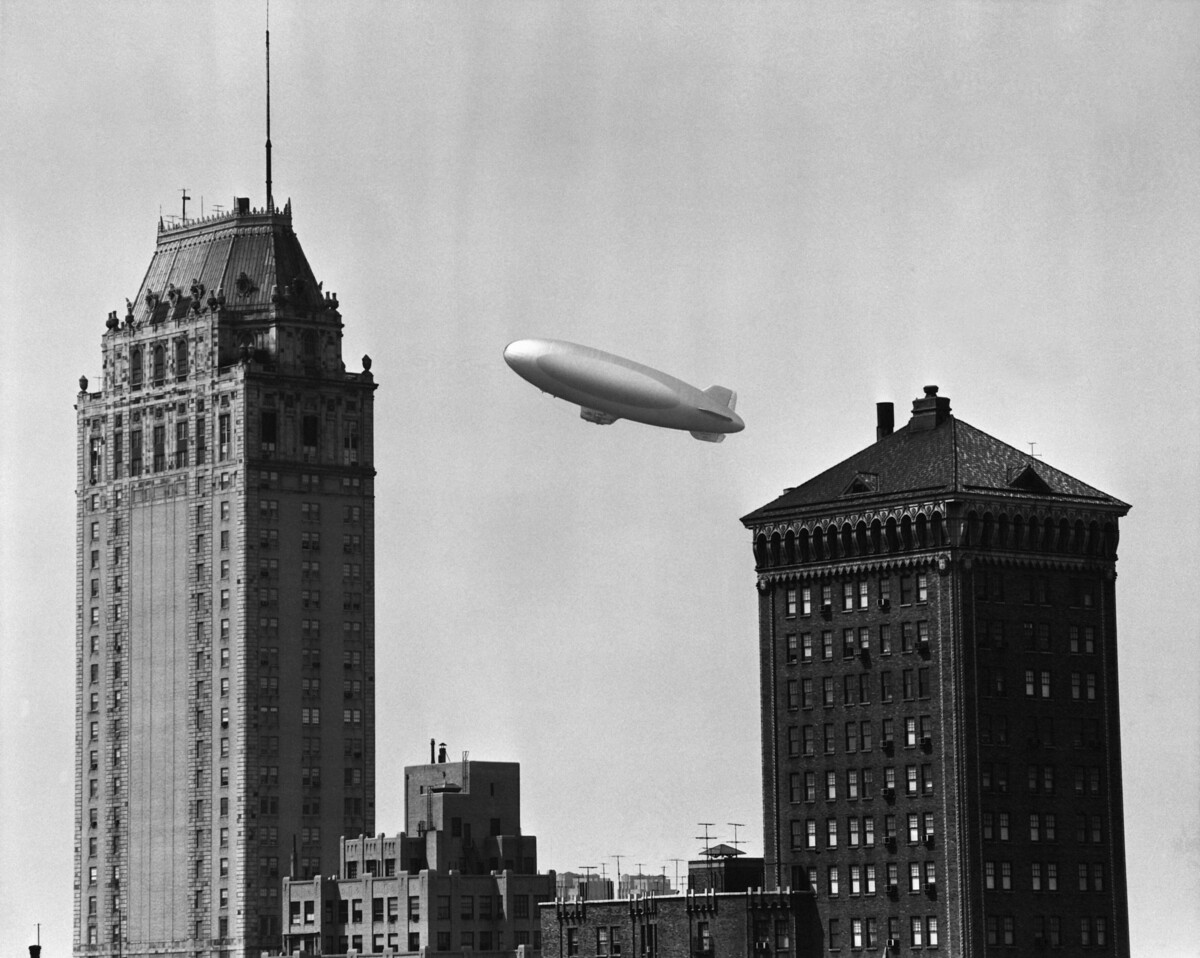  A blimp is pictured flying over a city circa 1950. 