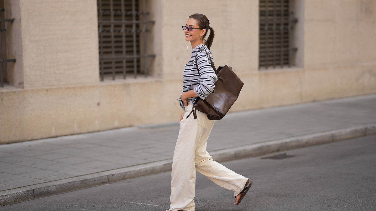 MUNICH, GERMANY - JUNE 8: Lina Uhrig is seen wearing a white cotton long sleeve top with black horizontal stripes, relaxed oversized silhouette and round neckline from Aritzia; white cotton wide leg jeans with a high waist and relaxed straight silhouette from H&M; brown flat leather flip flops with an open toe design from Havaianas; a natural pedicure visible through the open toe sandals; a dark brown grained leather shoulder bag with a compact silhouette, thin shoulder strap and minimal design from COS; gold tone hoop earrings and multiple gold tone rings; rectangular acetate sunglasses with dark tinted lenses from Kauf dich glücklich; white wired earphones; her dark brown hair is styled in a sleek low ponytail with a center part; with natural make up on June 8, 2026 in Munich, Germany. (Photo by Moritz Scholz/Getty Images)