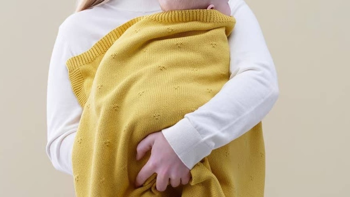 Woman holding baby in yellow blanket.