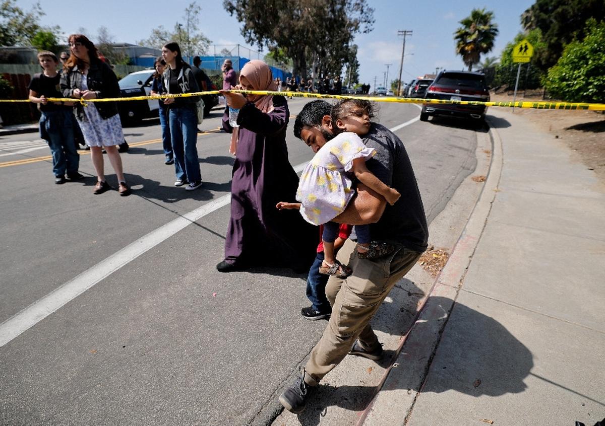 A parent passes under yellow tape cordoning an area, as he carries his child while they leave the mosque, at the scene of a shooting at the Islamic Center in San Diego, California, U.S., May 18, 2026.  REUTERS/Mike Blake