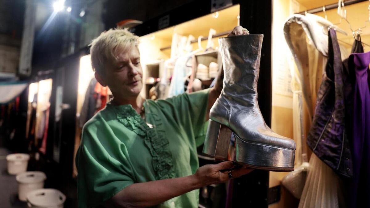 LOS ANGELES, CA - June 25, 2026: Eva Maciek, the travel costume supervisor of the show, holds up a pair of silver platform boots backstage at the Mamma Mia! theater production at the Ahmanson Theater in downtown Los Angeles on Thursday, June 25, 2026. (Christina House / Los Angeles Times)