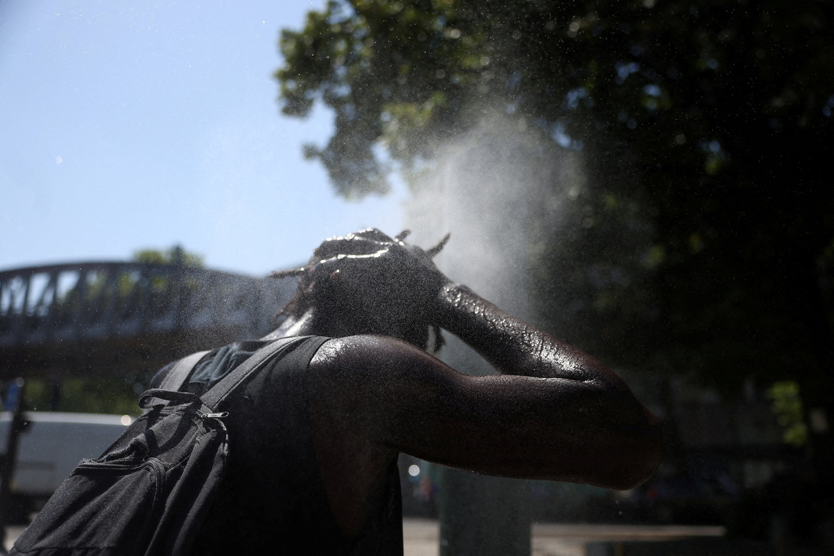 A person cools off at a water mister on a street in Paris as temperatures rise during a heatwave affecting a large part of France, June 22, 2026. REUTERS/Alice Sacco
