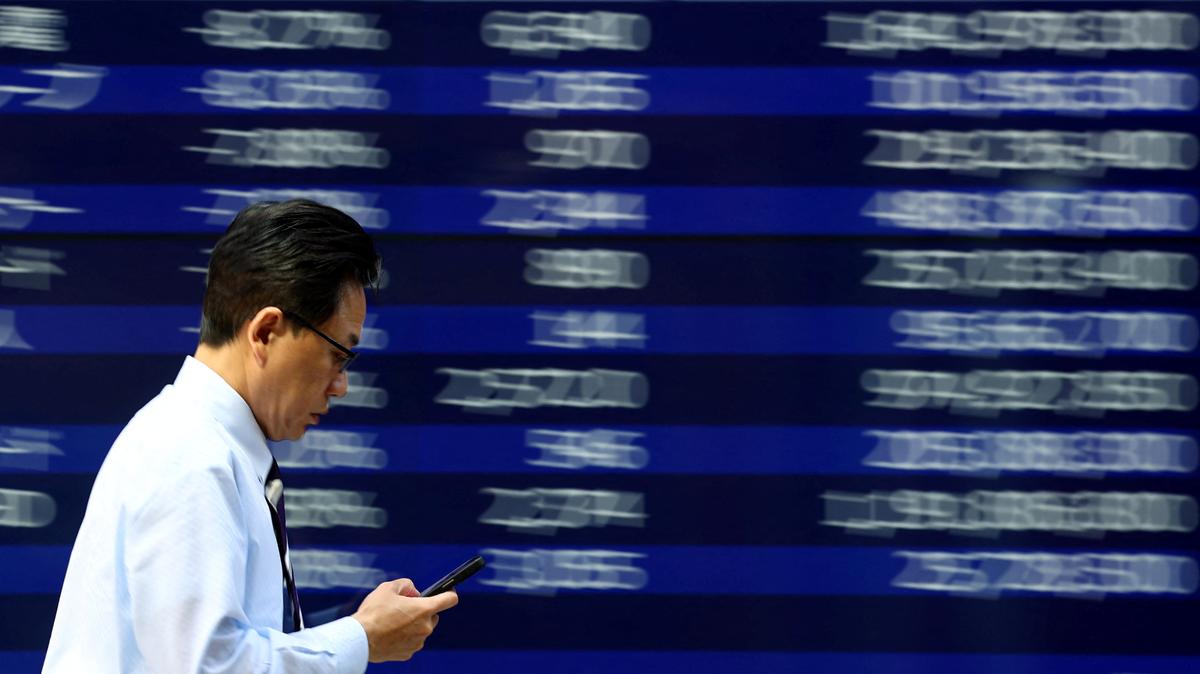 A man walks past an electronic screen displaying stock quotation board in Tokyo, Japan April 15, 2025. REUTERS/Issei Kato