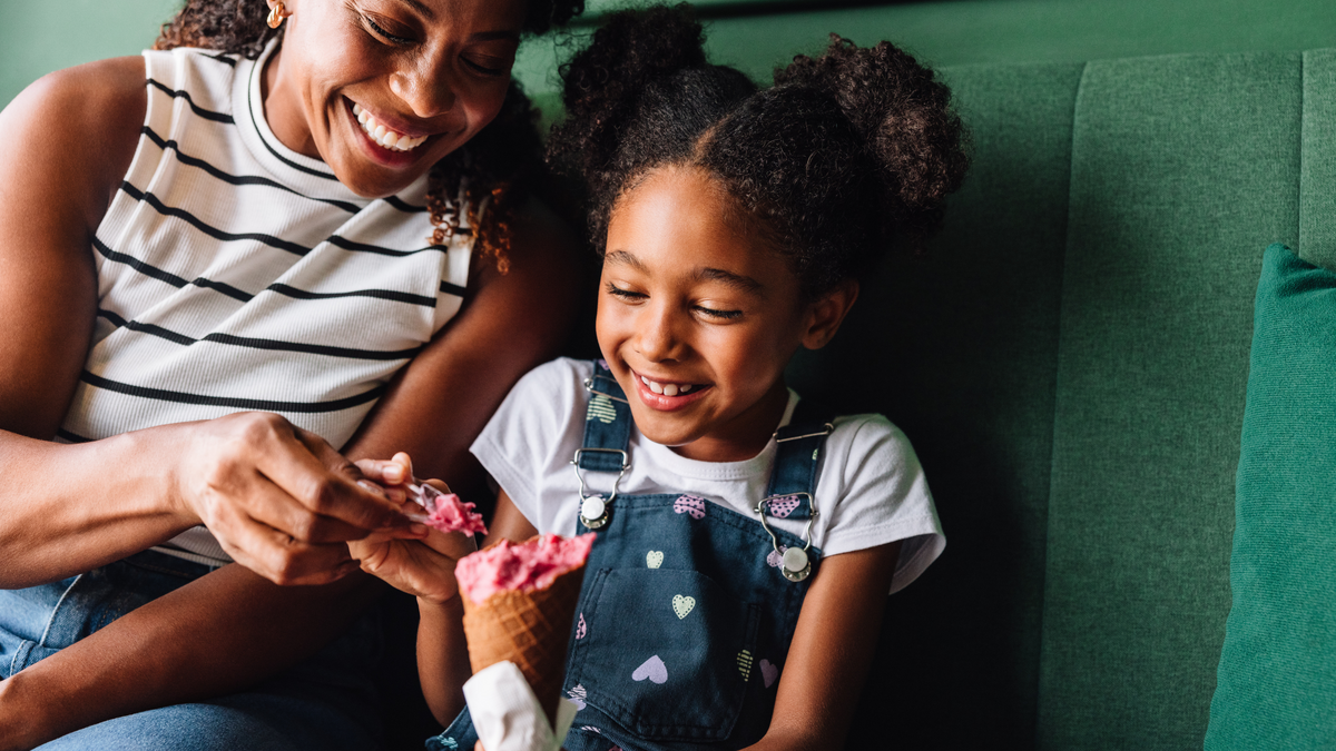 A joyful Black mother and her young daughter share ice cream. 