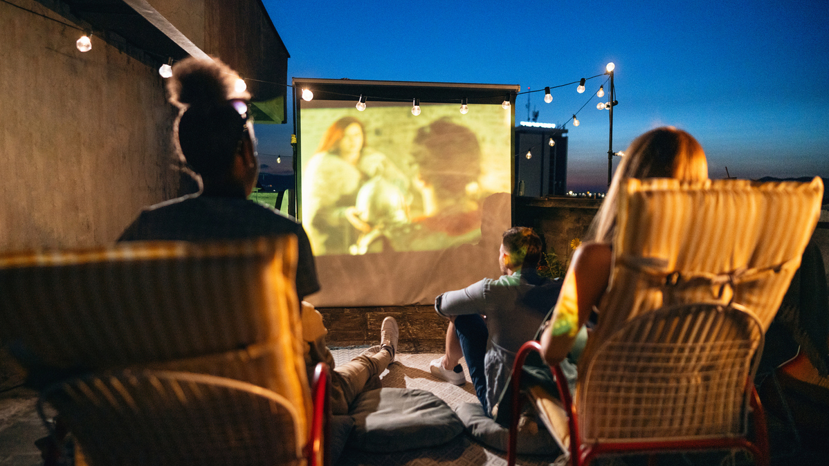 Group of unrecognizable multiracial young female and male friends, watching a movie on the rooftop