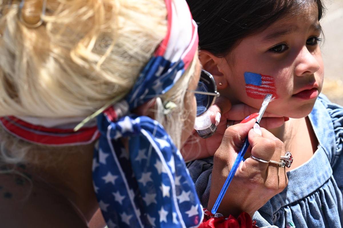 Sarah Jansson paints an American flag on the face of Nelsis Coronado, 4, during the Greeley Stampede's Independence Day parade in Greeley, Colo., July 4, 2026. America celebrates the 250th anniversary of its independence today, with people from one end of the country to the other marking the milestone with fireworks, parades and concerts. (Mark Makela/The New York Times)