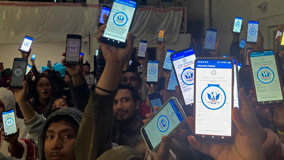 Decenas de migrantes muestran sus teléfonos el domingo 22 de enero de 2023 mostrando en ellos la app CBPOne, en un albergue en Tijuana, México. La aplicación de teléfono móvil para que los inmigrantes busquen asilo en Estados Unidos ha estado sobresaturada desde que se presentó este mes en uno de varios cambios importantes en la respuesta del gobierno estadounidense a flujos migratorios sin precedentes. Los migrantes se sienten cada vez más frustrados por una variedad de mensajes de error en la app. (AP Foto//Elliot Spagat)