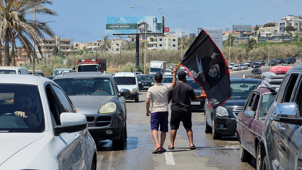 A man holding flags with the image of former Hezbollah leader Hassan Nasrallah walks on a road while traffic moves on a road as people head further south following the deal between the U.S. and Iran, in Sidon, Lebanon, June 18, 2026. REUTERS/Ali Hankir