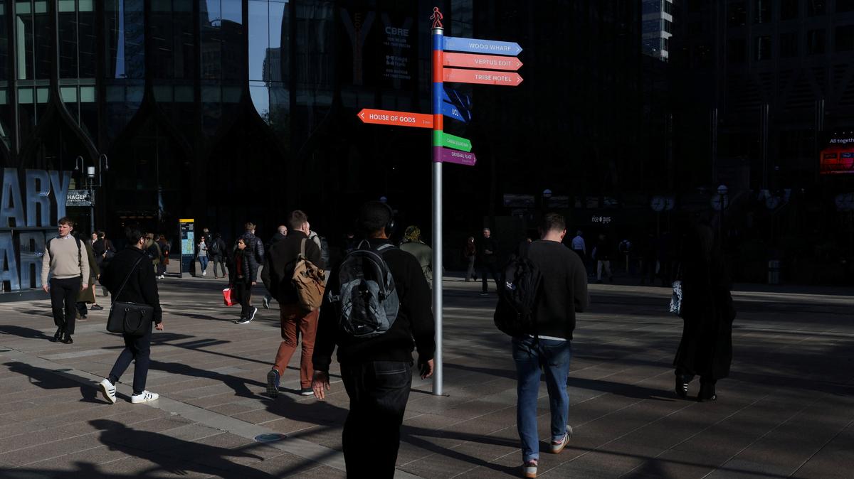 People walk past colourful signposts in the financial and business district of Canary Wharf, in London, Britain, April 13, 2026.  REUTERS/Kevin Coombs