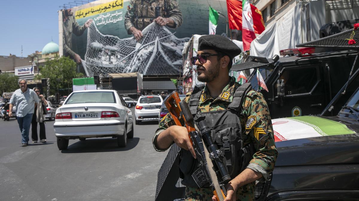 An Iranian police office stands on patrol near a poster depicting Iranian soldiers holding a net in the shape of the Strait of Hormuz, with U.S. military aircraft ensnared in a fishing net, on May 9, 2026, in Tehran, Iran. There is little sign of progress in negotiations between Iran and the United States, despite both sides' insistence that their monthlong ceasefire is holding. (Majid Saeedi/Getty Images/TNS)