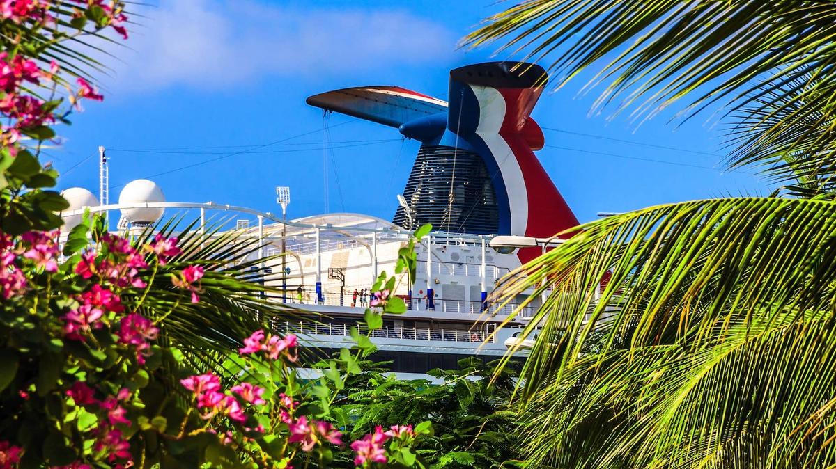 Carnival Vista cruise ship funnel viewed through a opening in green plants with red flowers and palm trees in Ocho Rios, Jamaica. 