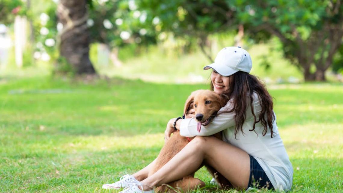 Woman sitting in the grass hugging her dog.