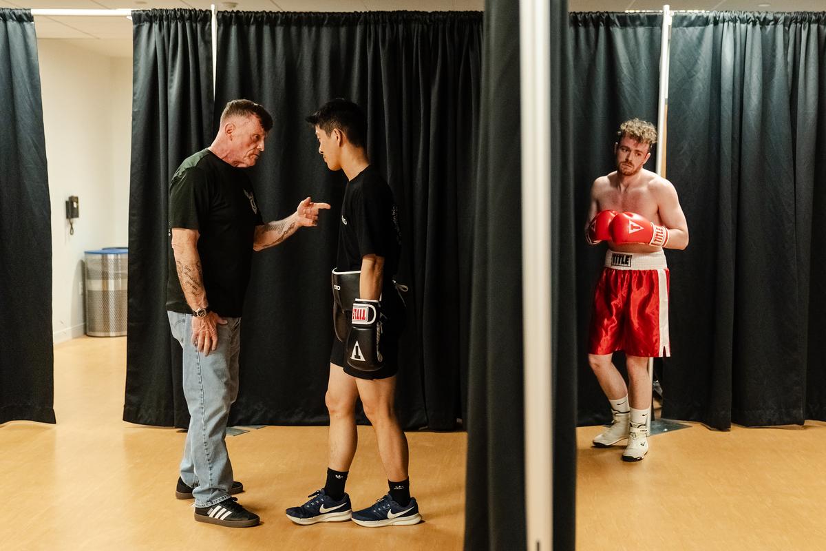 Harvard Boxing Club coach Joe Lake gives a pep talk to freshman Ryan Jiang as his opponent, Colin Brazas, right, a senior from the Babson Boxing Club, warms up before a bout at Babson College in Wellesley, Mass., April 24, 2026. Boxing clubs at Harvard and other colleges are drawing new members as students look for a real-life connection. (Sophie Park/The New York Times)