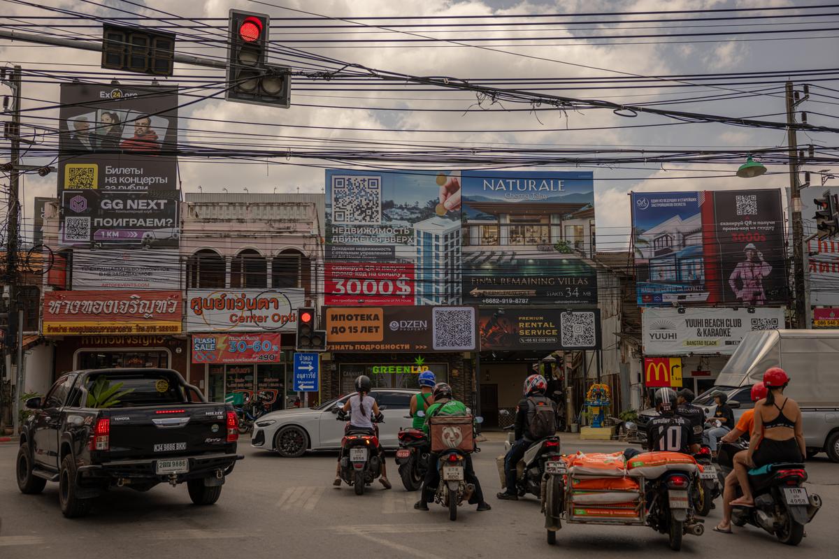 Motorists drive past billboards in Thai, English and Russian in Phuket, Thailand on March 9, 2026. Thousands who fled Russia after the invasion of Ukraine have built an enclave in Phuket, where an air of impermanence hangs over their community. (Lauren DeCicca/The New York Times)..