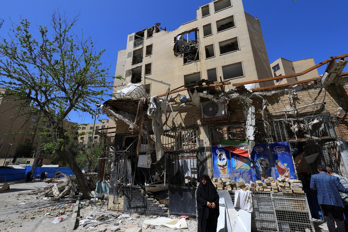 A woman stands next to debris lying in front of a residential building damaged by a strike on March 4, in Tehran, Iran, April 14, 2026. REUTERS/Thaier Al Sudani/File Photo