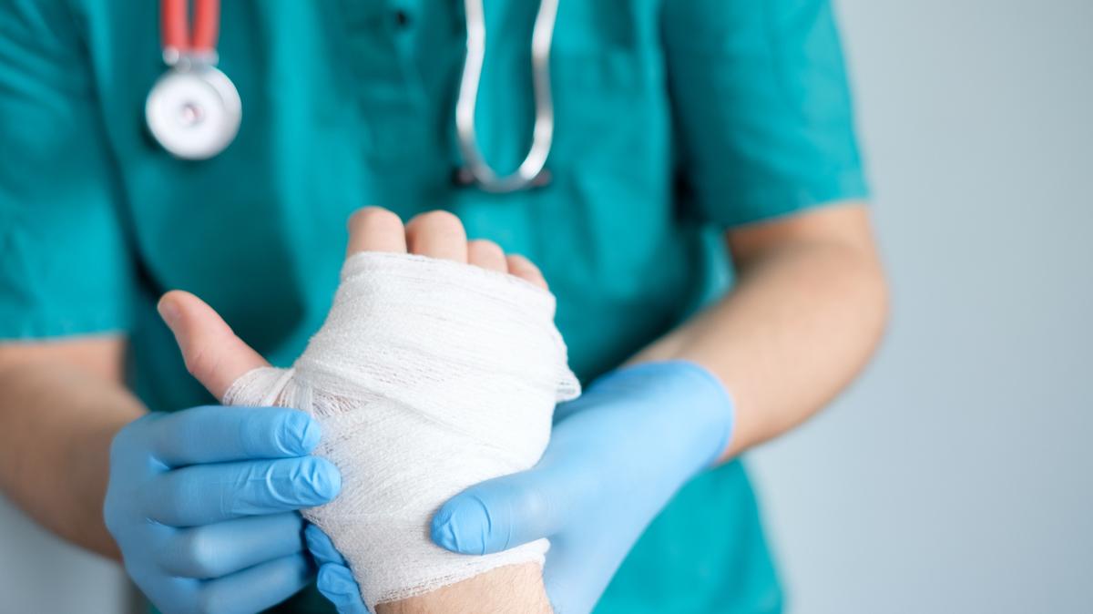 This is a stock photo of a patient’s bandaged hand being examined by a doctor.