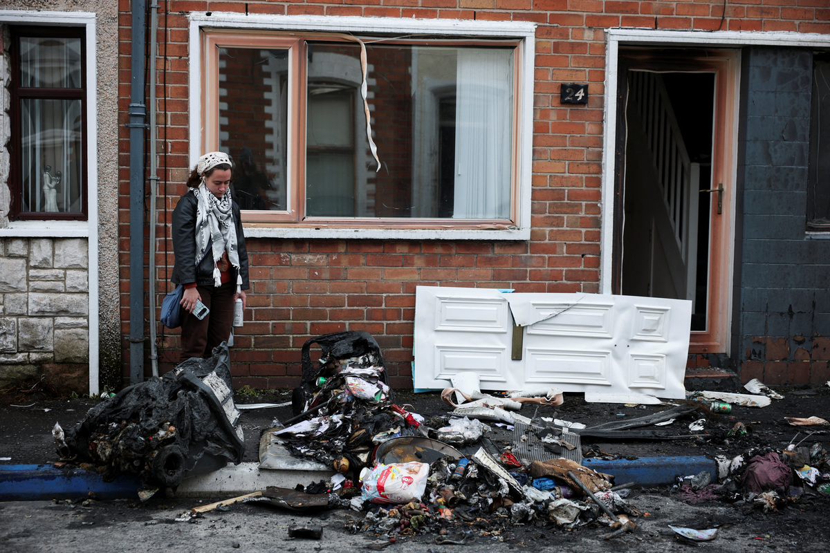 A resident looks at the charred debris scattered on the street in her neighbourhood, in the aftermath of anti-immigrant protests following a knife attack on June 8, which left a man seriously injured and prompted police to declare a critical incident, at Lendrick street, east Belfast, Northern Ireland, June 10, 2026. REUTERS/Isabel Infantes