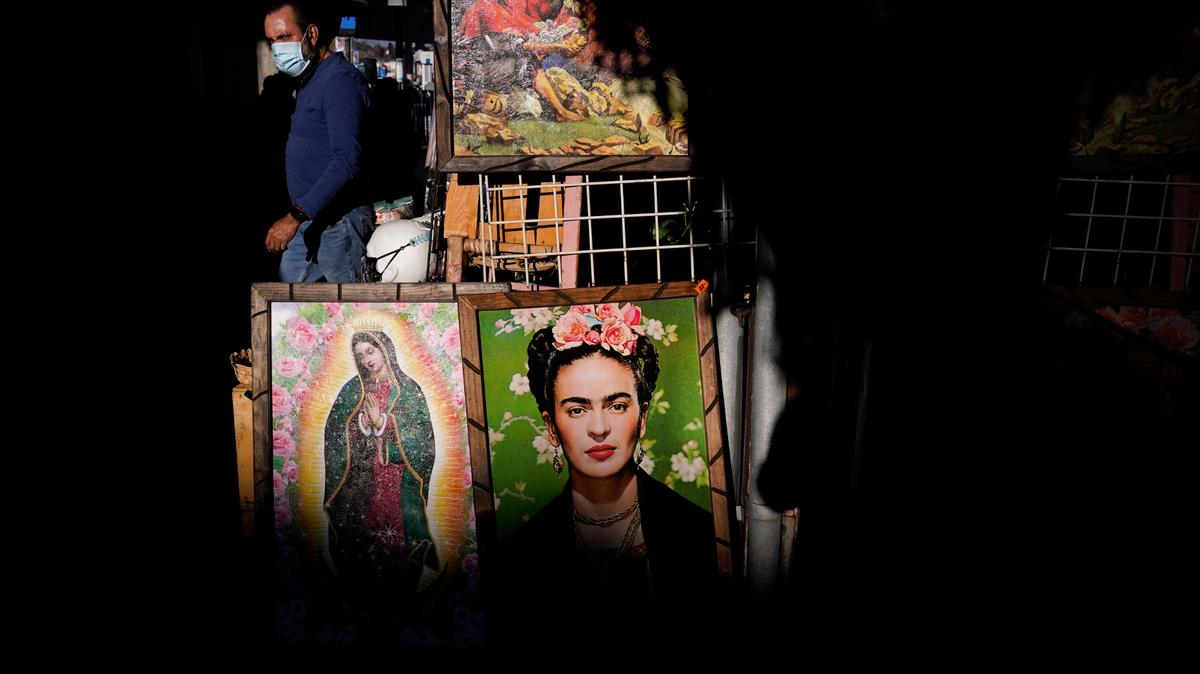 Framed paintings depicting Our Lady of Guadalupe and Mexican artist Frida Kahlo are placed outside a gift shop on Olvera Street in downtown Los Angeles, Wednesday, Dec. 16, 2020. The tree-covered brick alley typically teeming with tourists is empty. Many of the shops that sell everything from traditional Mexican folk dresses to paintings of artist Frida Kahlo to sombreros are padlocked and the ones open have few, if any, customers. (AP Photo/Jae C. Hong)