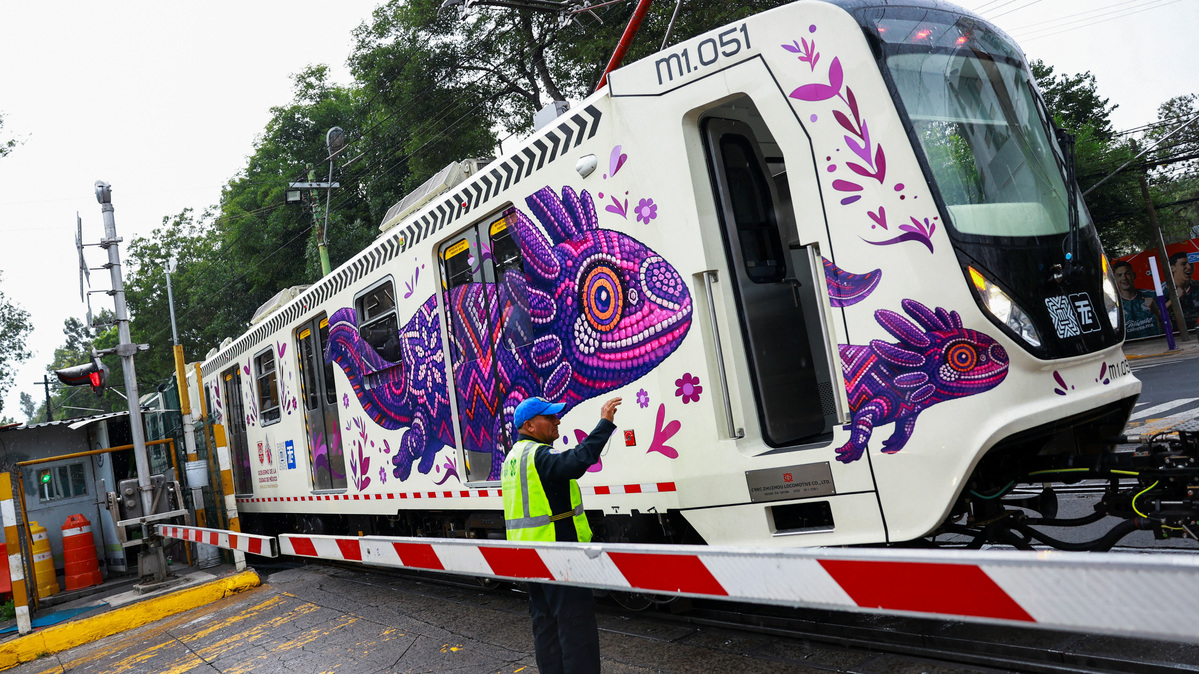 A crossing keeper gestures as a train car featuring an image of the critically endangered axolotl, a salamander native to central Mexico's lakes, passes by, in Mexico City, Mexico, May 27, 2026. The use of axolotl in public imagery ahead of the FIFA World Cup 2026 has divided residents who say more should be done to protect its habitat. REUTERS/Raquel Cunha     TPX IMAGES OF THE DAY