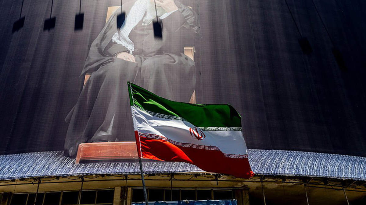 An Iranian flag is waved under a billboard of former Supreme Leader Ayatollah Ali Khamenei on Monday in Tehran. According to reports, the U.S. and Iran have signed a preliminary agreement to end the war and open the Strait of Hormuz.