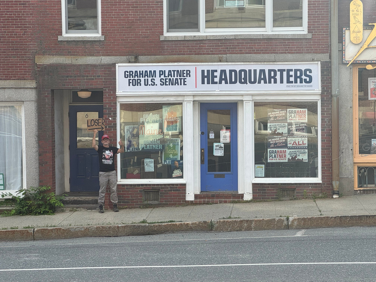Jeff McLain holds a sign that says "LOSER" outside of Graham Platner's office in Ellsworth, Maine.