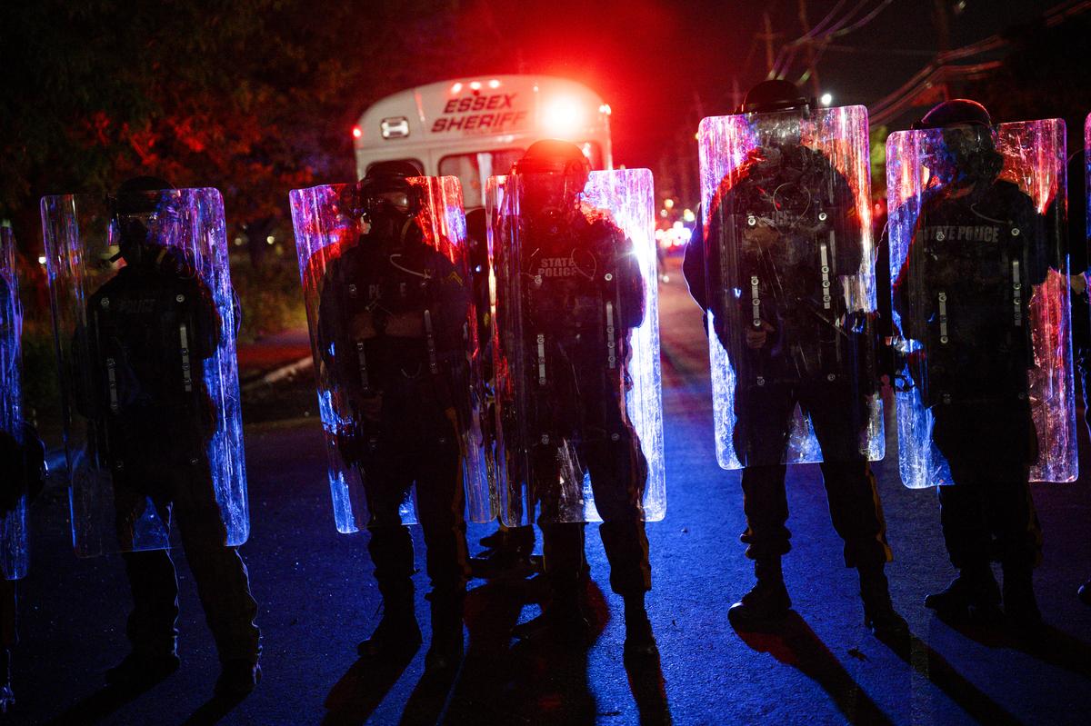 Police officers in riot gear monitor the anti-ICE demonstrations and counterprotests outside the Delaney Hall immigration detention center in Newark, N.J., May 30, 2026. Mayor Ras Baraka of Newark imposed a curfew early Sunday around the immigration detention center after a second consecutive night of unrest over living conditions there. (Vincent Alban/The New York Times)